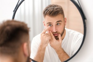 Man putting on his contact lenses in front of a mirror