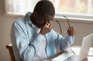 Man sitting at desk removing his glasses to rub eyes.